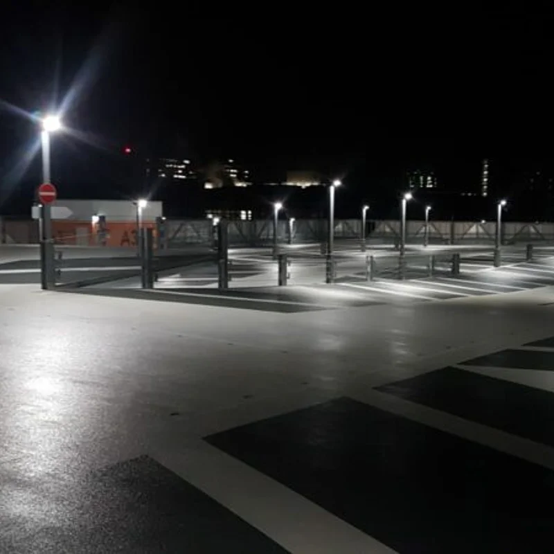 Beschichtetes Parkdeck bei Nacht mit Markierungen, Beleuchtung und geparkten Fahrzeugen.