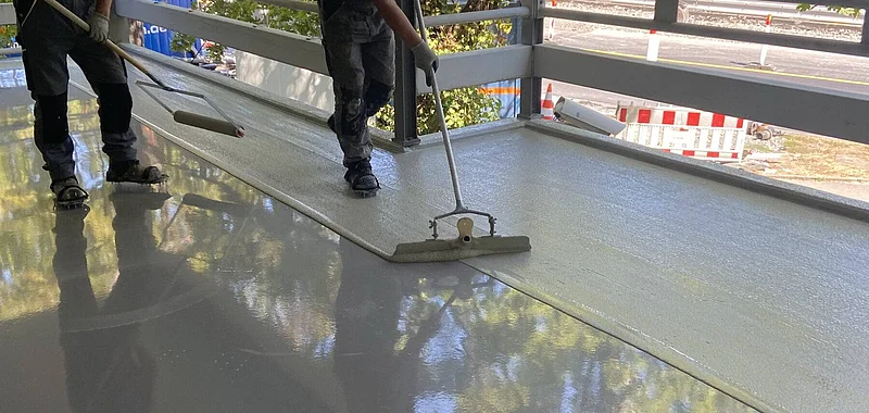 Arbeiter überbeschichten eine glänzende Parkhausfläche mit Rollen, die frische Beschichtung ist noch nass.
